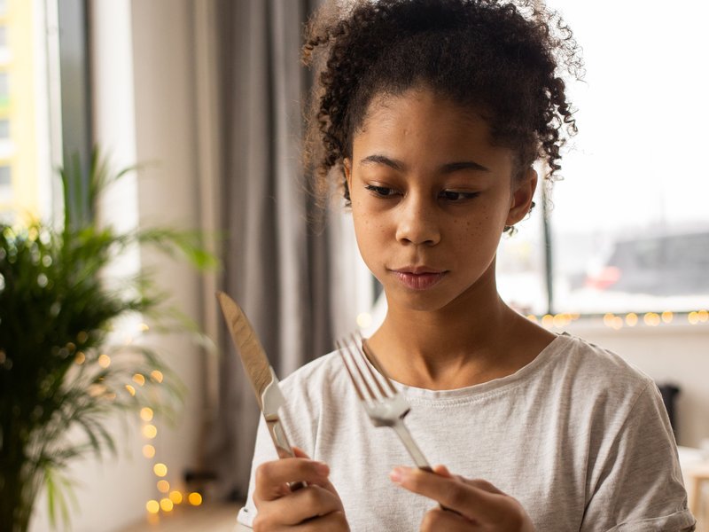 A young girl learning to hold a knife and fork at a set place